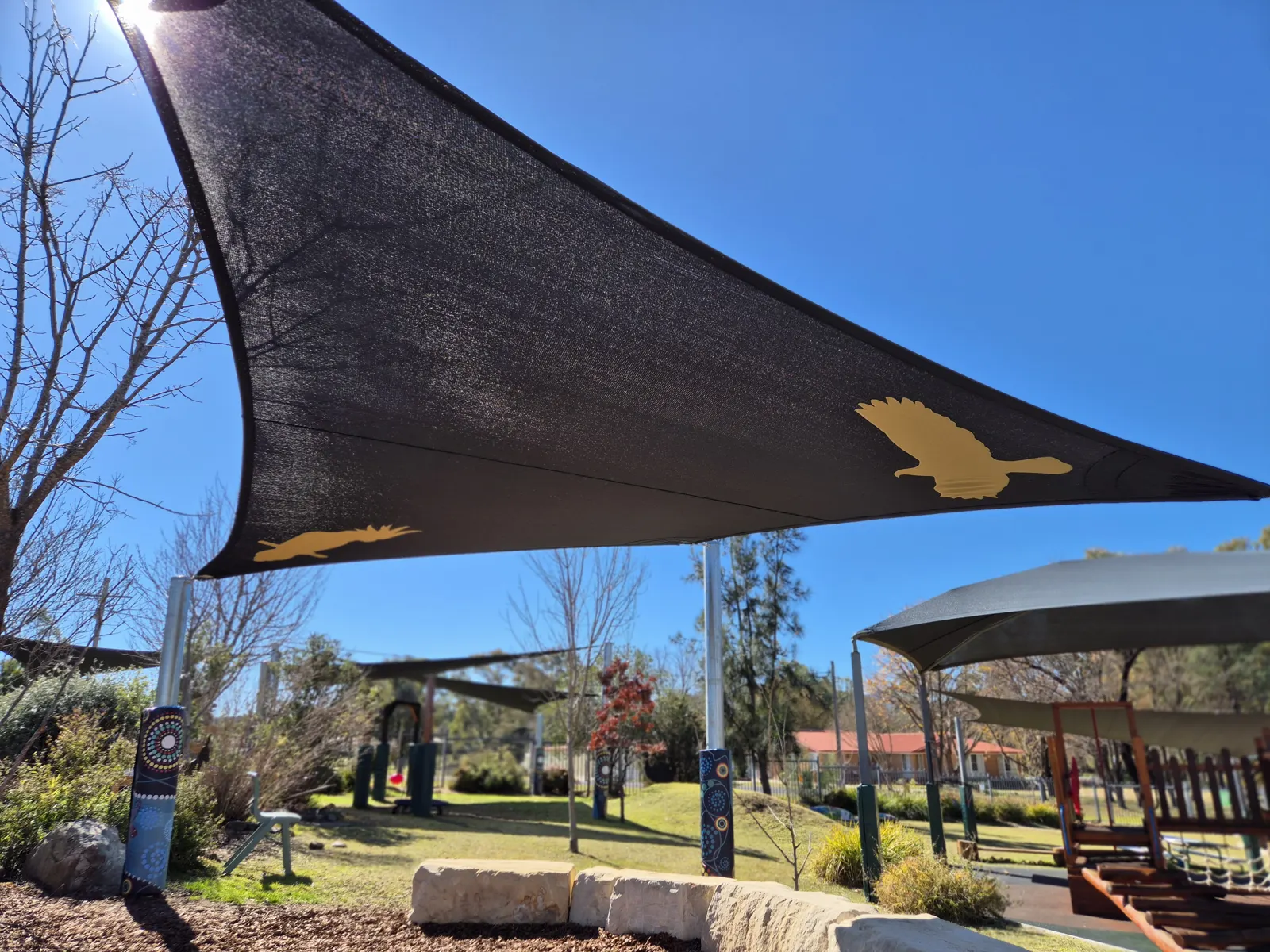 Black shade sail with gold bird designs shading a natural playground area - New England Shade Sails, Tamworth