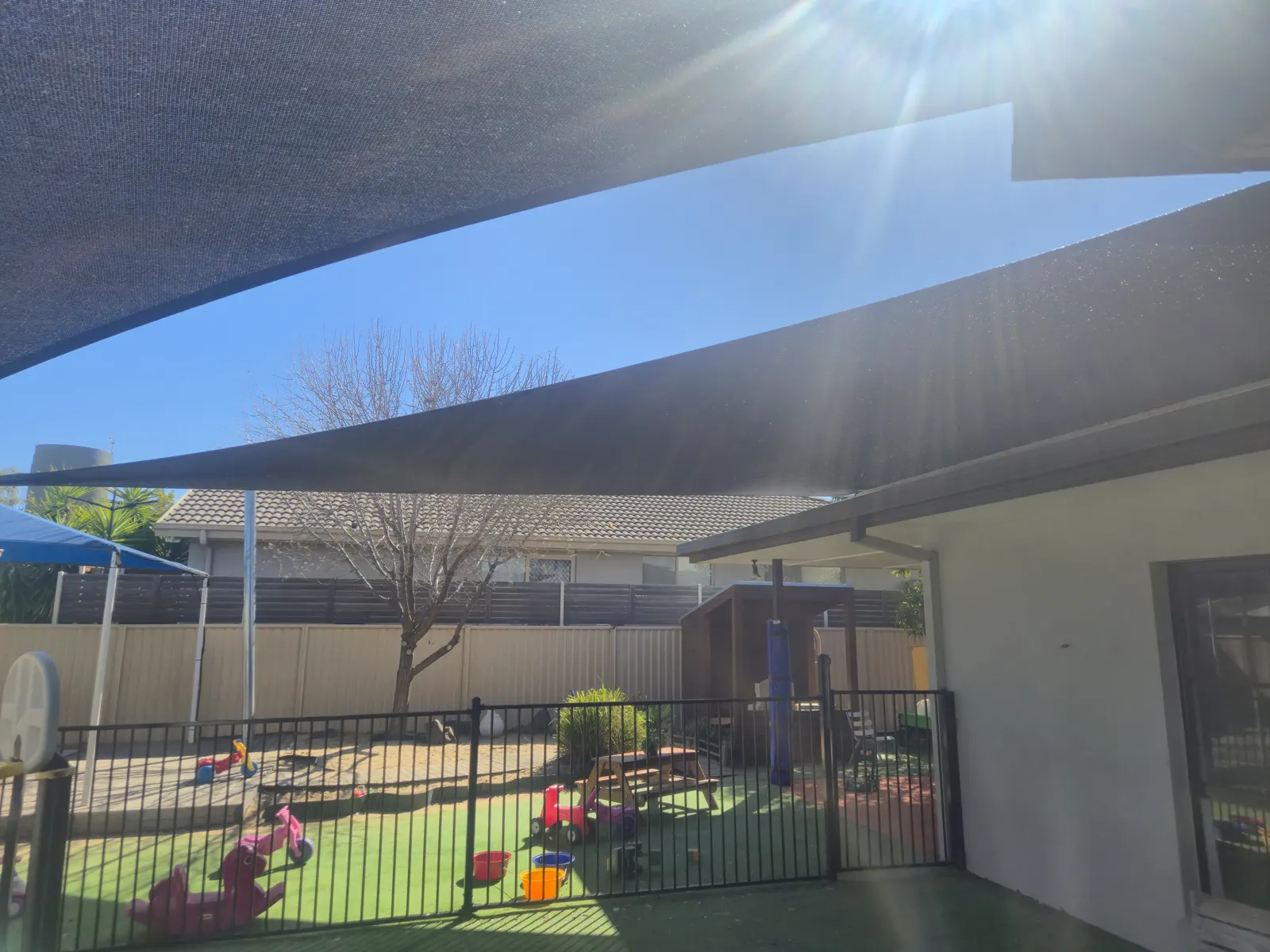 Charcoal shade sail extending over a fenced childcare courtyard with outdoor toys - New England Shade Sails, Tamworth