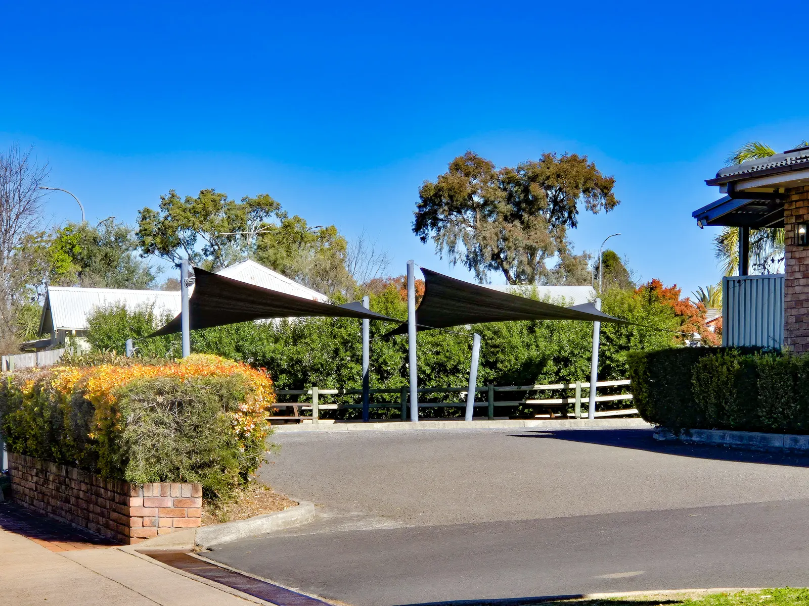 Two charcoal shade sails on steel posts beside a paved carpark entry - New England Shade Sails, Tamworth