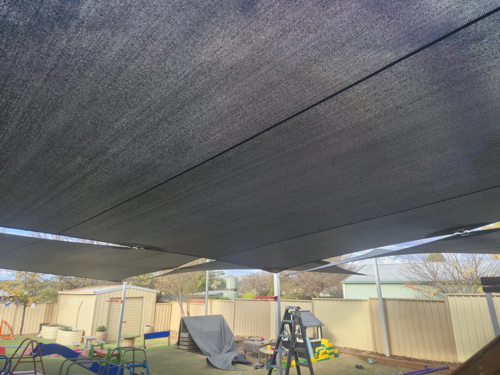 Charcoal shade sails covering a fenced childcare yard with play equipment and artificial turf - New England Shade Sails, Tamworth