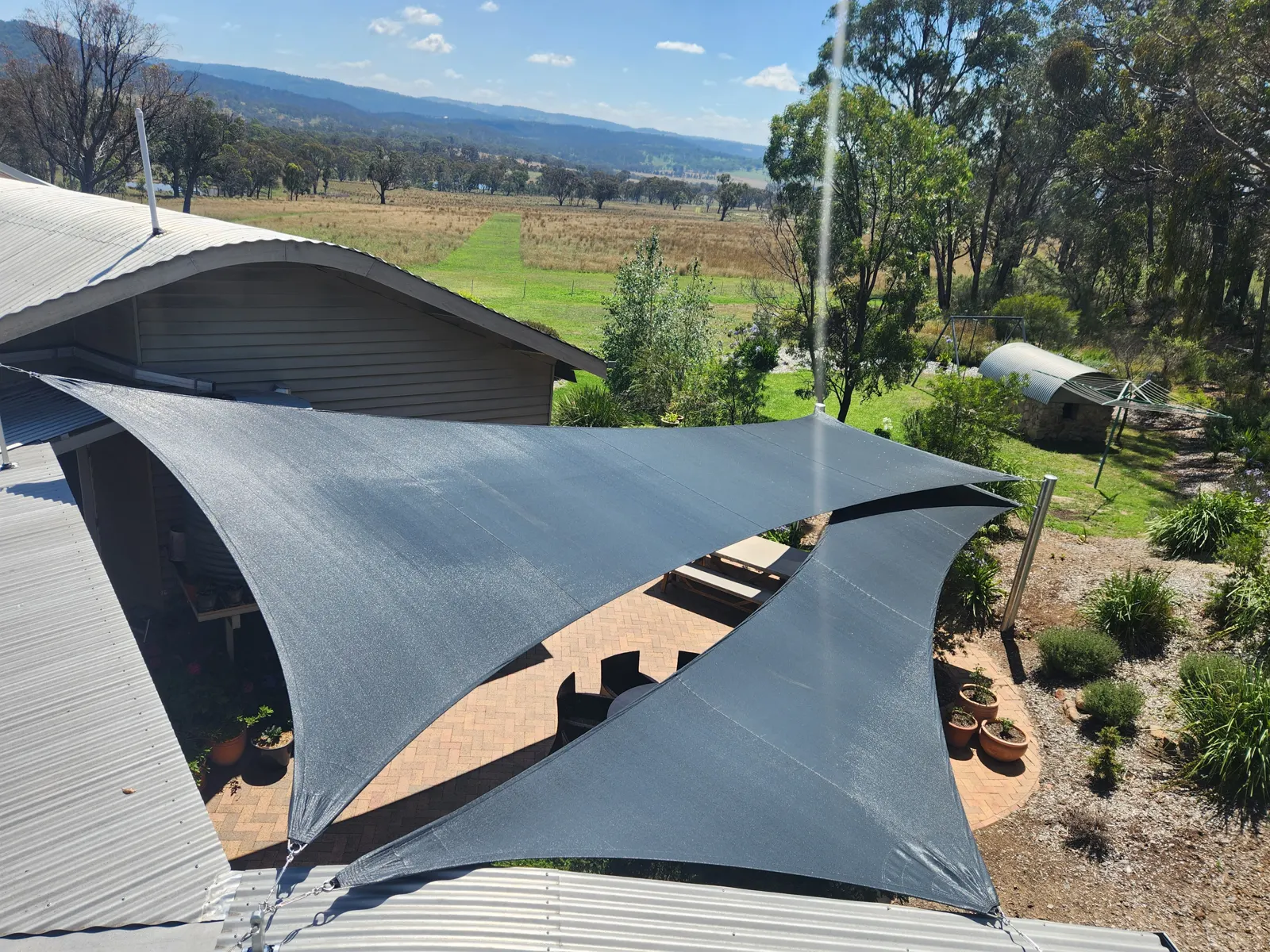 Charcoal shade sails covering a paved patio beside a rural home with valley views - New England Shade Sails, Tamworth