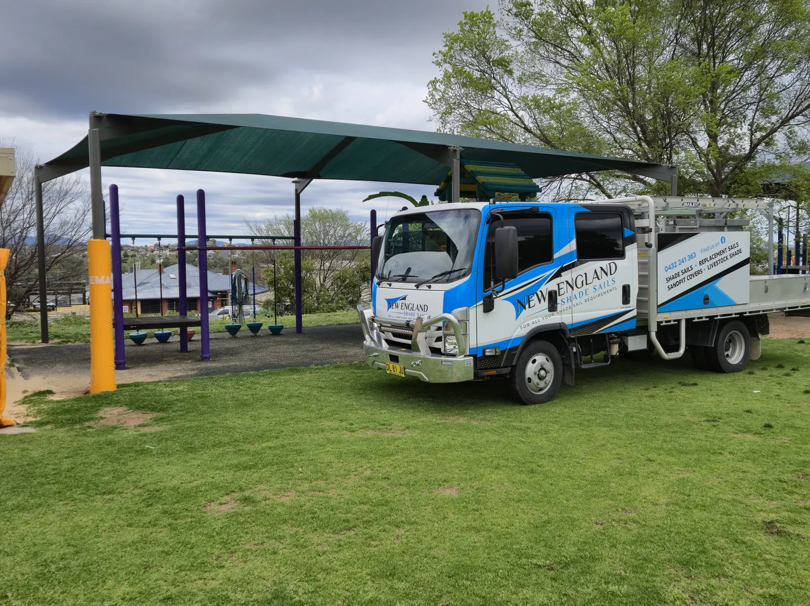 Green shade structure over a park playground with the company work truck parked nearby - New England Shade Sails, Tamworth