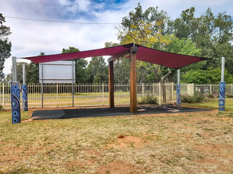 Maroon shade sail on steel posts beside a school play field - New England Shade Sails, Tamworth