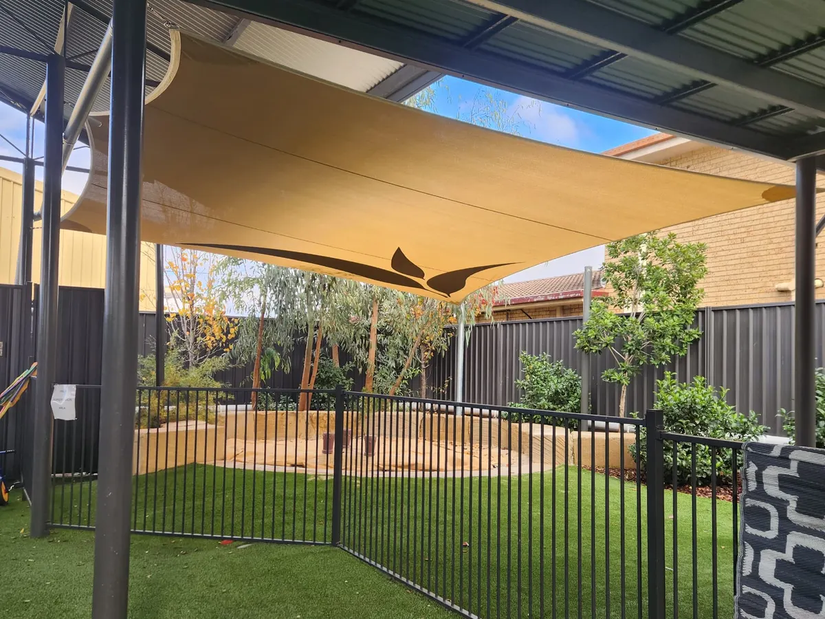 Sand-coloured shade sail with a leaf print covering a fenced childcare sandpit - New England Shade Sails, Tamworth