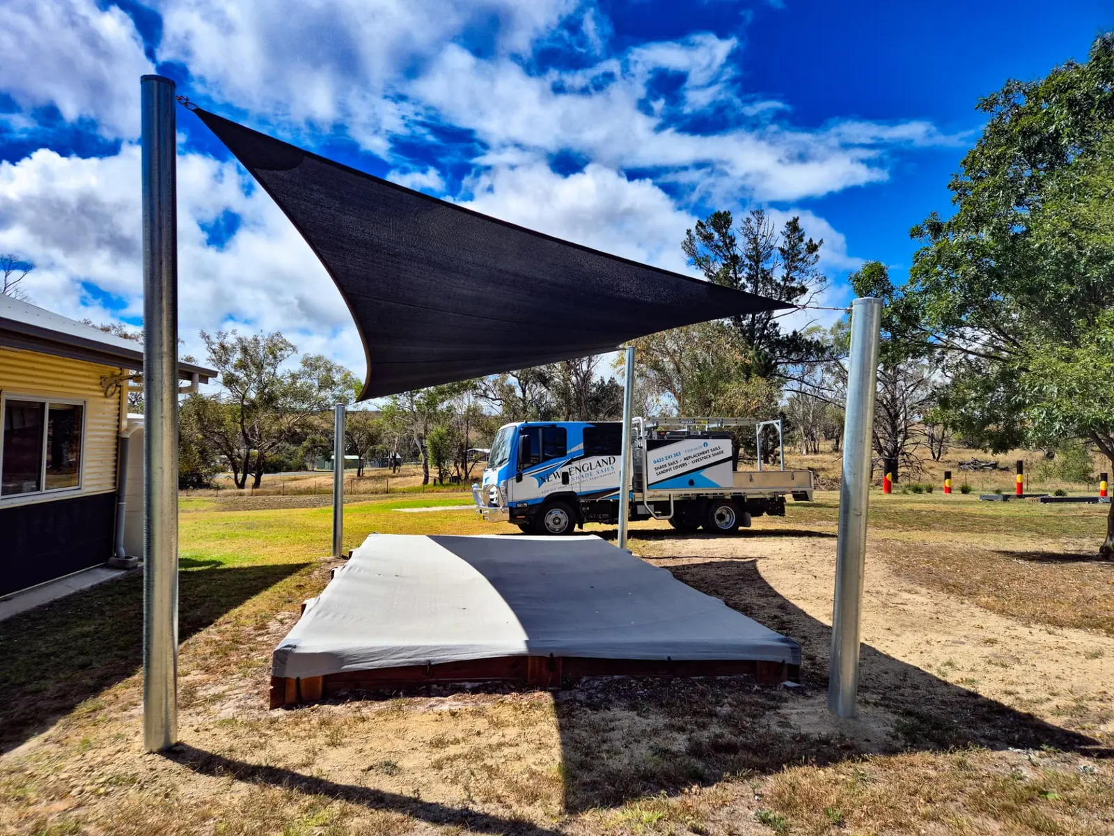 Black triangular shade sail shading a covered timber sandpit beside a weatherboard building - New England Shade Sails, Tamworth