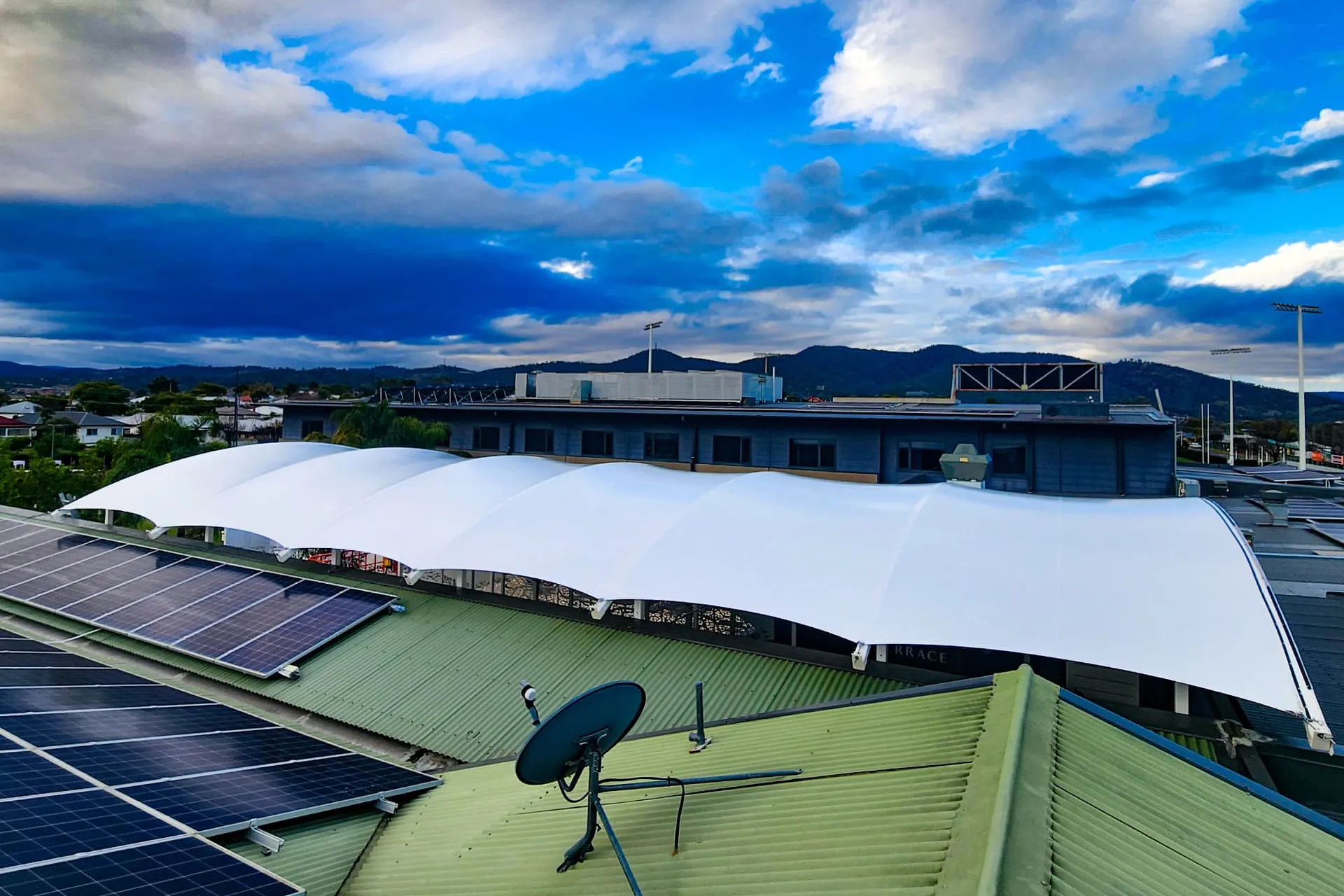 White tension shade sail structure over a rooftop with hills and blue sky behind - New England Shade Sails, Tamworth