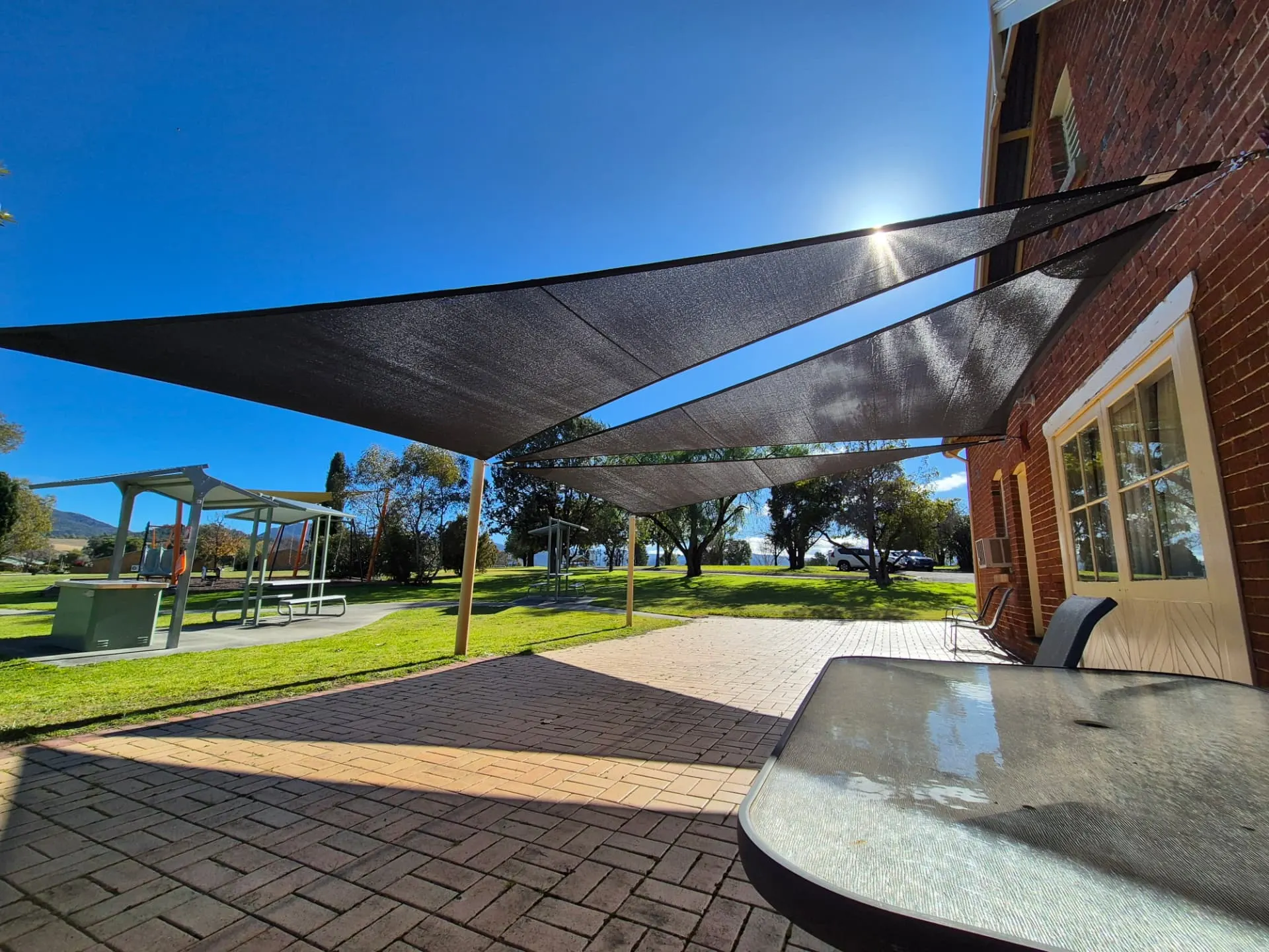 Charcoal shade sails tensioned over a brick-paved outdoor area beside a heritage brick building - New England Shade Sails, Tamworth