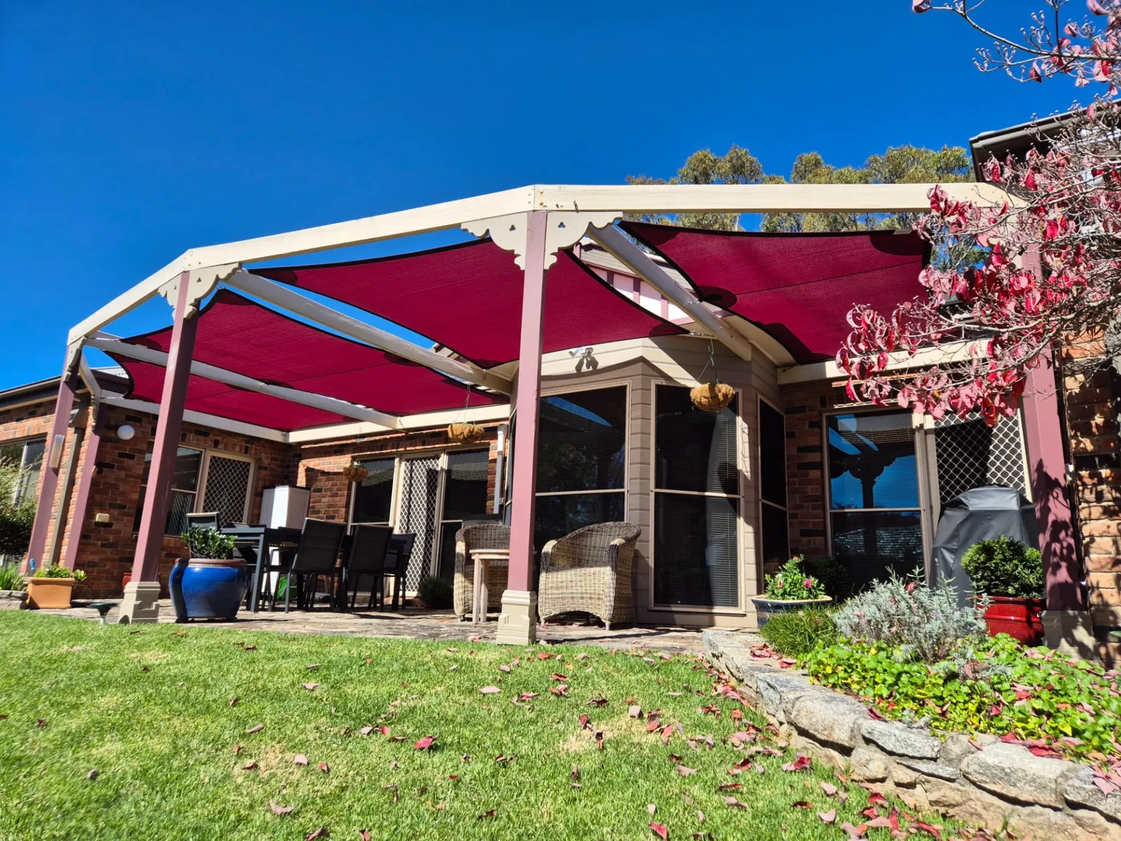 Maroon shade sails tensioned tightly across a timber pergola over a backyard patio - New England Shade Sails, Tamworth